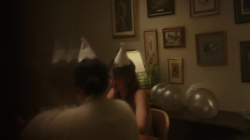 People sitting at a table talking and wearing birthday party hats
