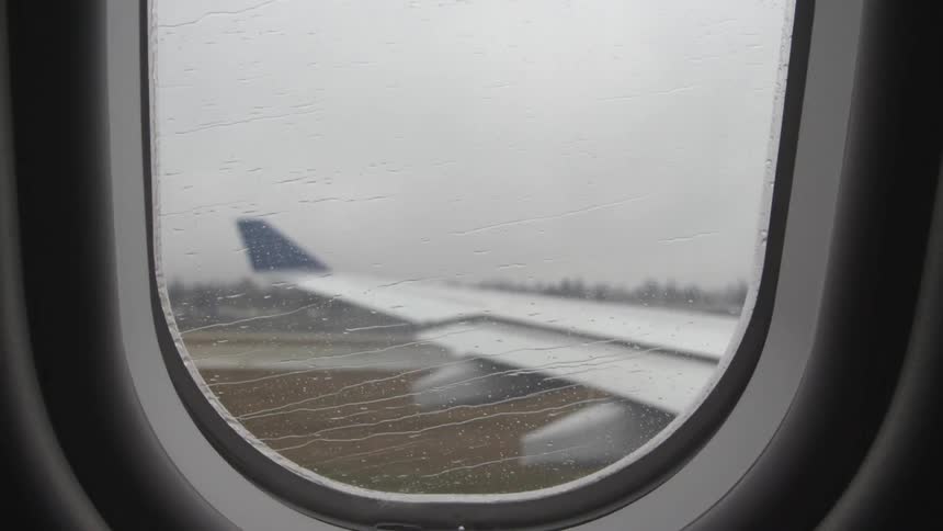 Rain hits airplane window as it travels down a runway