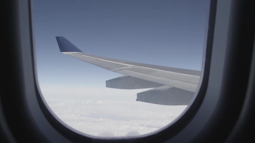 Outside a plane window the clouds are seen below