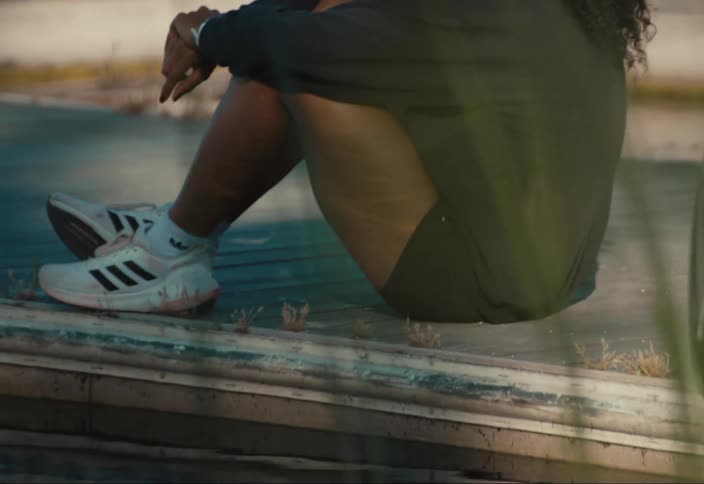 A woman wearing hearing aids sits on a dock by the water with her reflection mirrored below