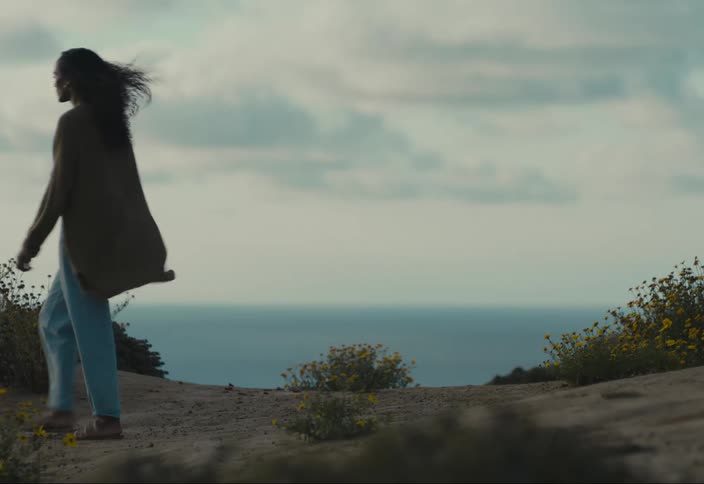 A woman walks along the edge of a cliff gazing out over the vast expanse of the ocean