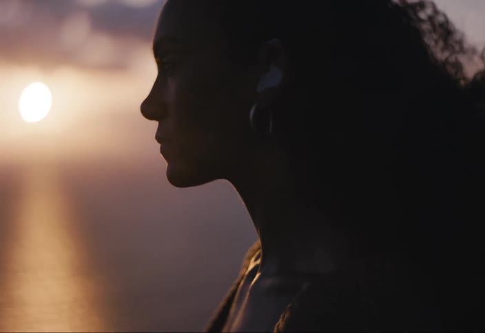 A woman wearing hearing aids looks out at the ocean as the sun sets