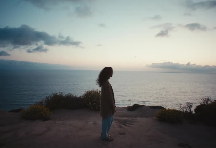 A woman stands atop a cliff over the ocean