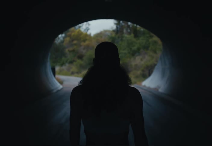 A woman is walking on a road through a tunnel with trees along the roadside