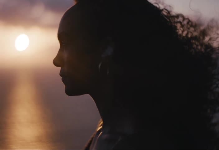 Portrait of a woman in an outdoor setting with the sea beside and the sun on the horizon