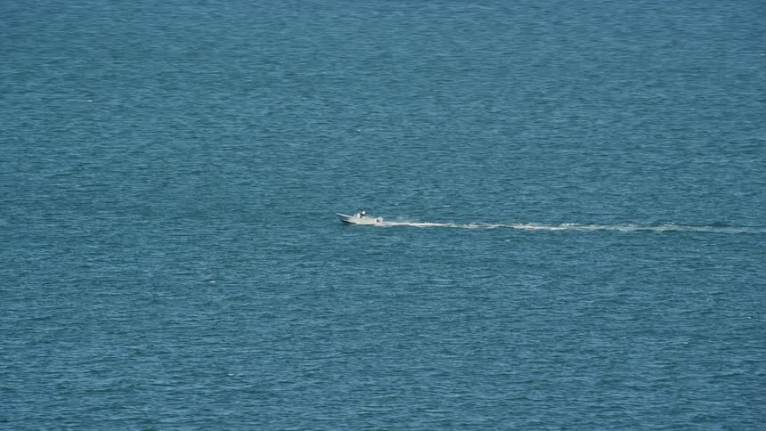 A small boat leaves a trail of splashing water behind as it speeds across the lake