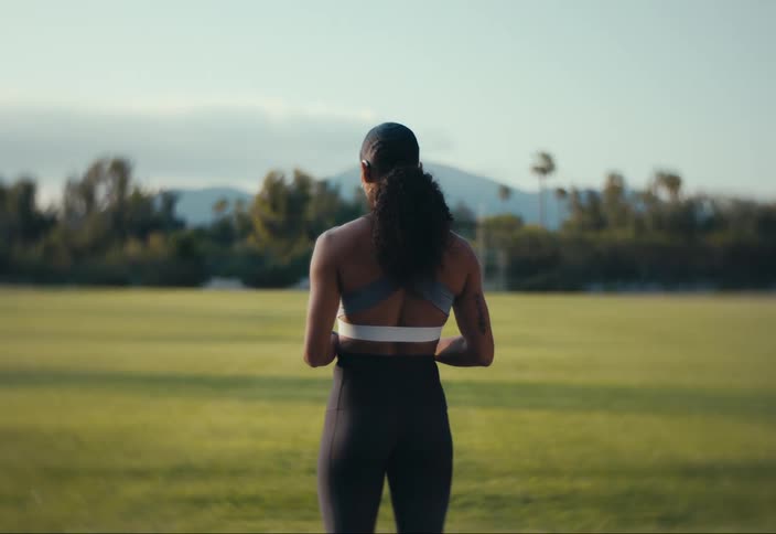 A woman in athletic clothes standing and looking forward to where there is a grass field