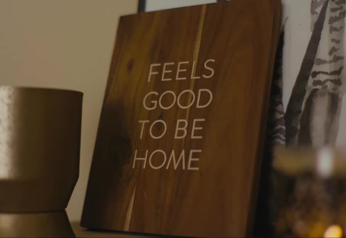 A wooden sign in a room reads feels good to be home