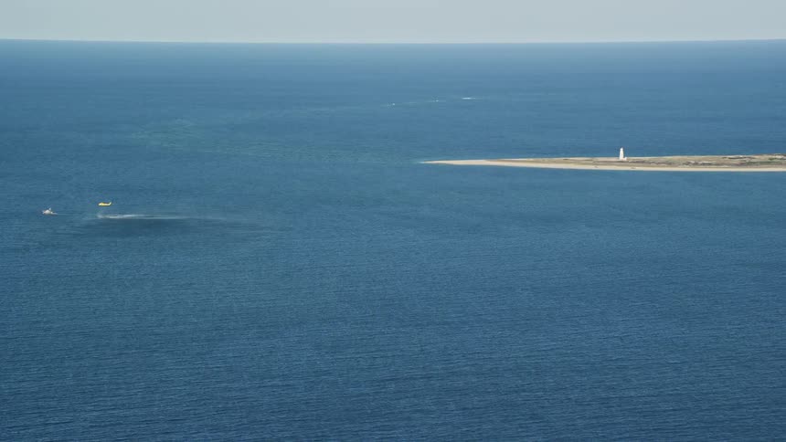 From an aerial perspective a boat and a helicopter are seen just off the shoreline