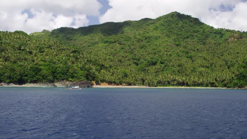 A boat sailing down a wide body of water next to grassy hills
