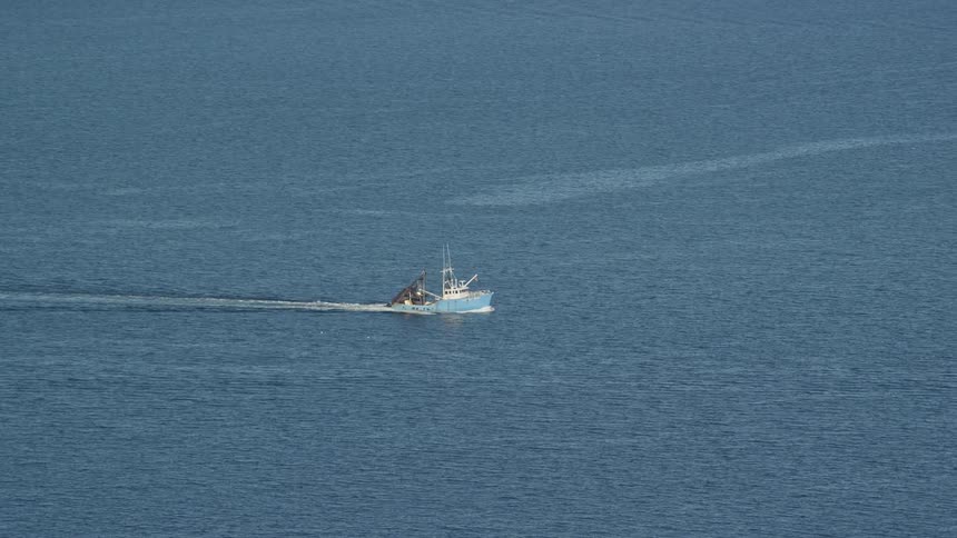 Aerial view of light blue fishing boat sailing across water
