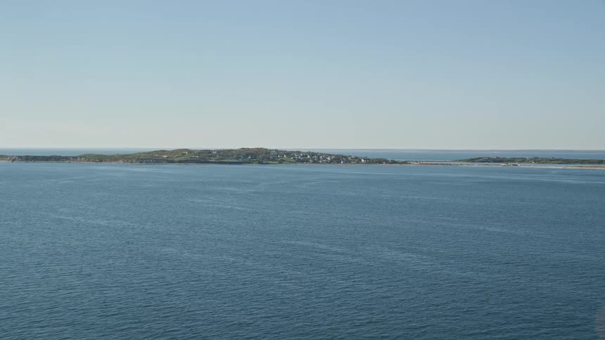 Aerial panorama of the sea with an island on the horizon containing residences