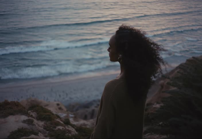 A young woman with hearing aids standing on a cliff close to the beach as the wind blows
