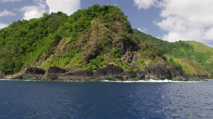 A large mountain with trees and a body of blue water with a few clouds in the sky