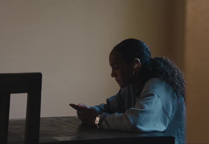 A woman sits at a table texting on her phone