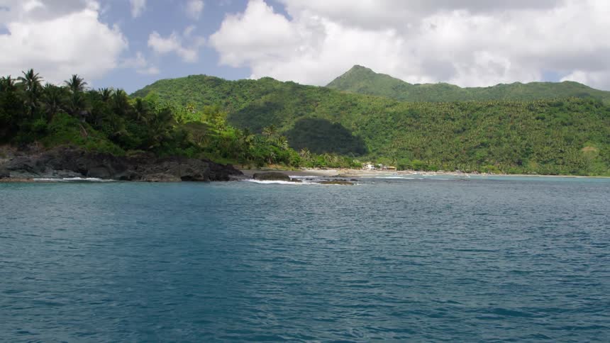 A large body of rippling water with mountains and trees and fluffy white clouds in the sky