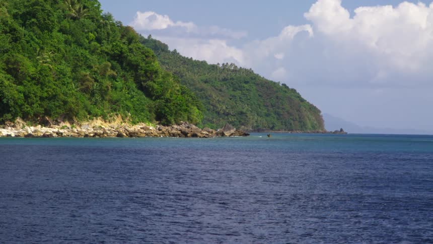 A large body of water on a bright day with clouds in the sky and mountains covered in trees