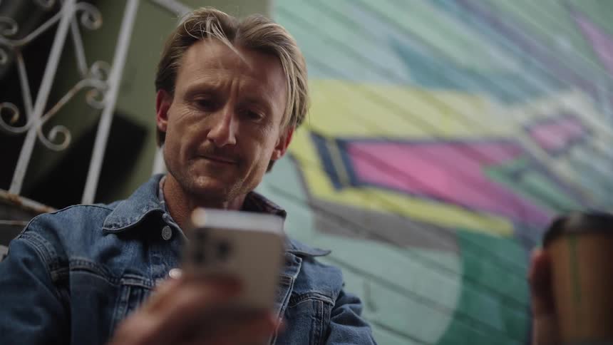 A man is drinking from a cup as he uses his cell phone
