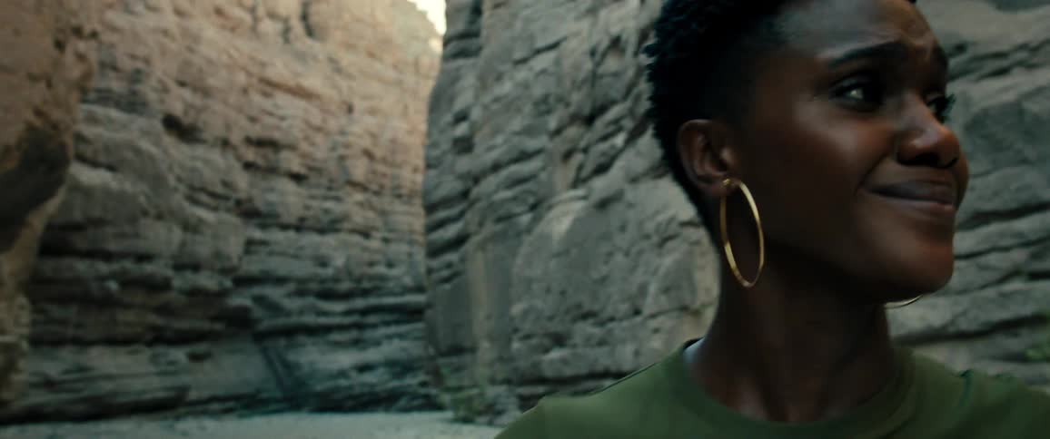 Worried and sad woman with short hair hoop earrings and a green shirt stands between the towering walls of a canyon