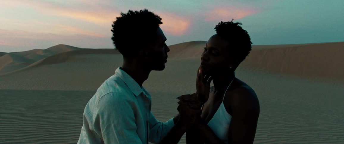 Man and woman gazing romantically at each other in the desert dunes at sunrise