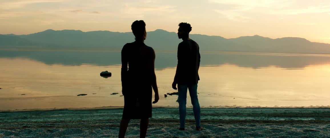 Silhouettes of two people standing along the coast