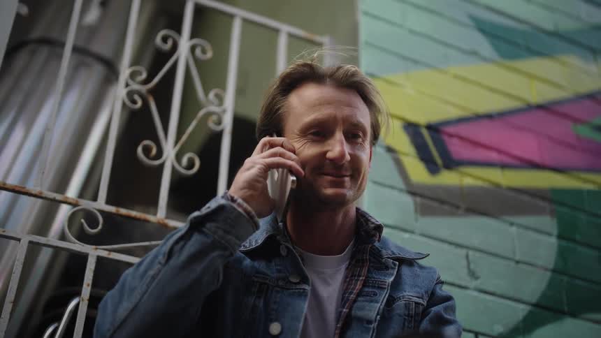 A man talking on phone at midday with his back against the wall