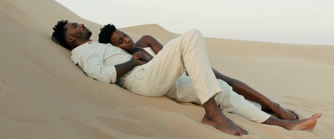 A man and a woman lay on the sand at midday