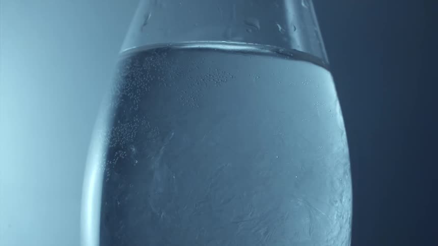 A glass bottle with water inside and outside there are drops of water