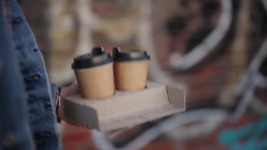 Hand of a person walking and carrying a package with 2 coffees