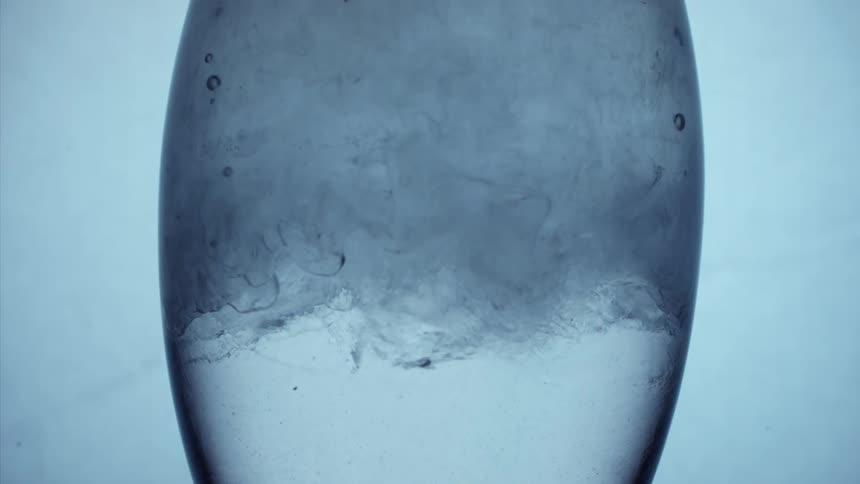 Bubbles float among cloudy dye entering top of eggshaped transparent container