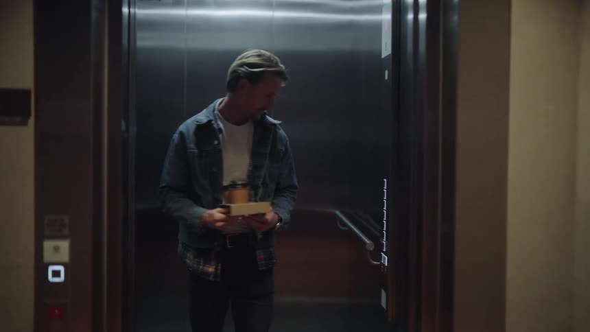 A man is carrying a tray with two cups of coffee as he gets into an elevator