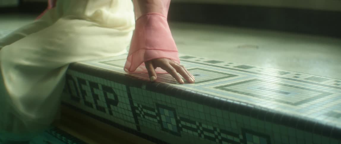 A woman sits on a ledge with a tiled pattern indoors rubbing her hand on the surface