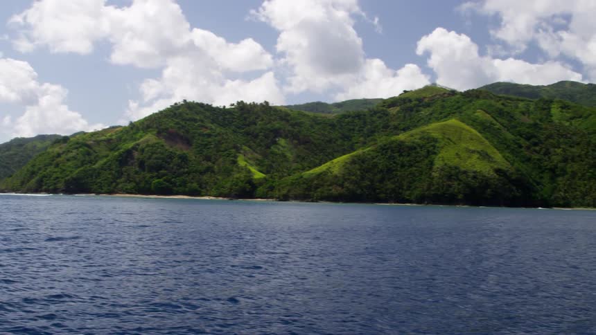 A large body of water surrounded by mountains and trees on a bright day with clouds