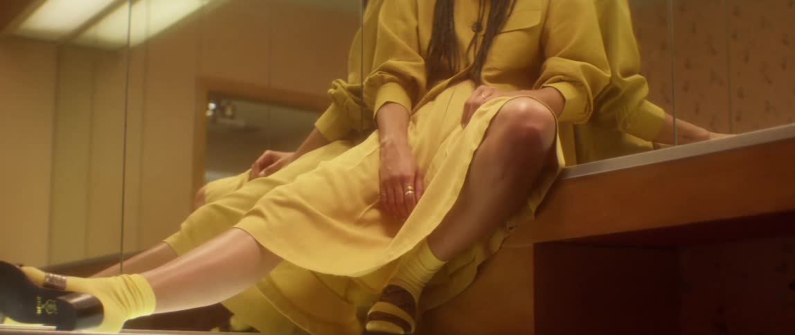 Person wearing yellow socks and dress sits on counter leaning against mirror