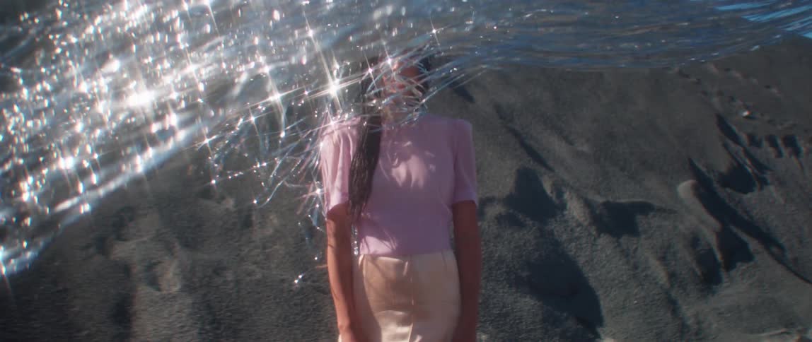 A woman stands still in the desert as silver tinsel blows and shines in front of her