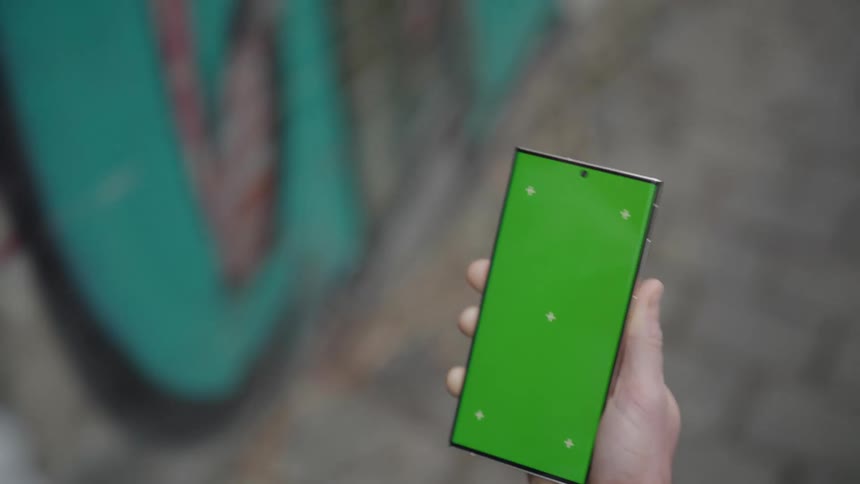 A person walking while holding a cell phone with the screen all green