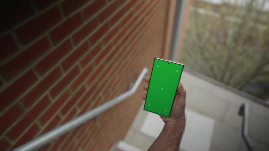 A man in a crisp white sweater descends the apartment stairs clutching a smartphone in his hand