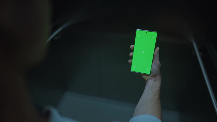 A man is holding a phone with a green screen as he walks into an elevator