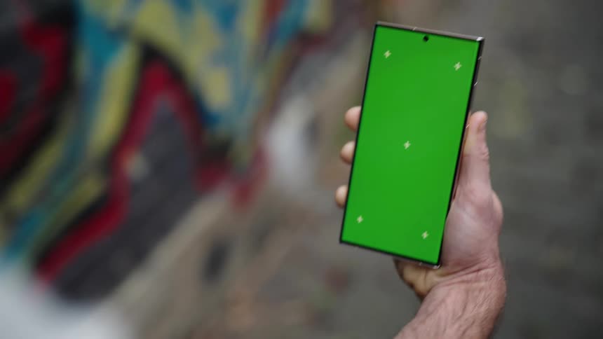 Man viewing a smartphone walks past building covered by graffiti style mural