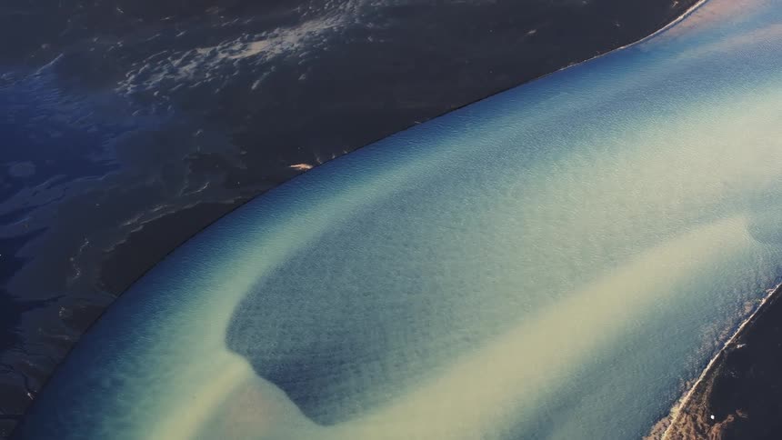 Aerial of blue sea with dark sand coast