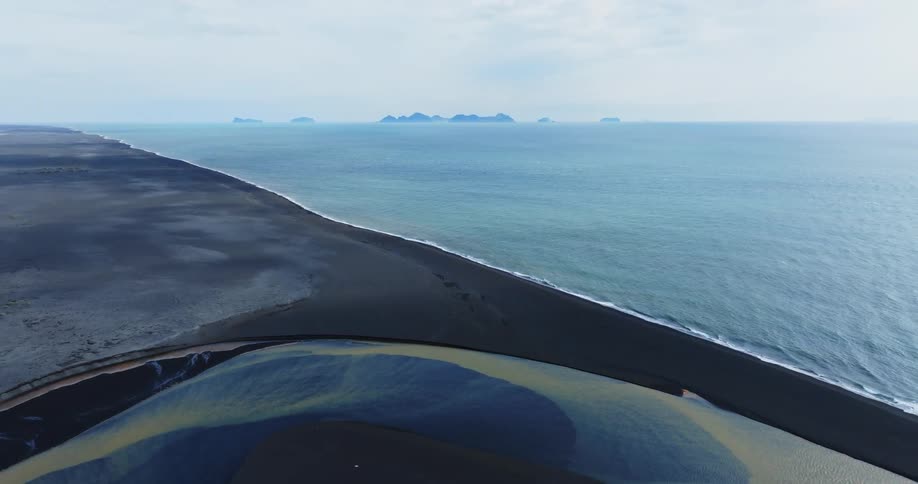Aerial view of a blue and yellow river with a black sand beach