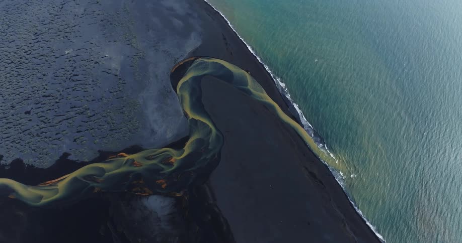 A colorful river on the black sand beach finds its way into the ocean