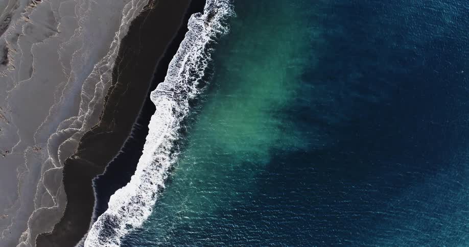 Clear water waves roll into shore and over the black beach