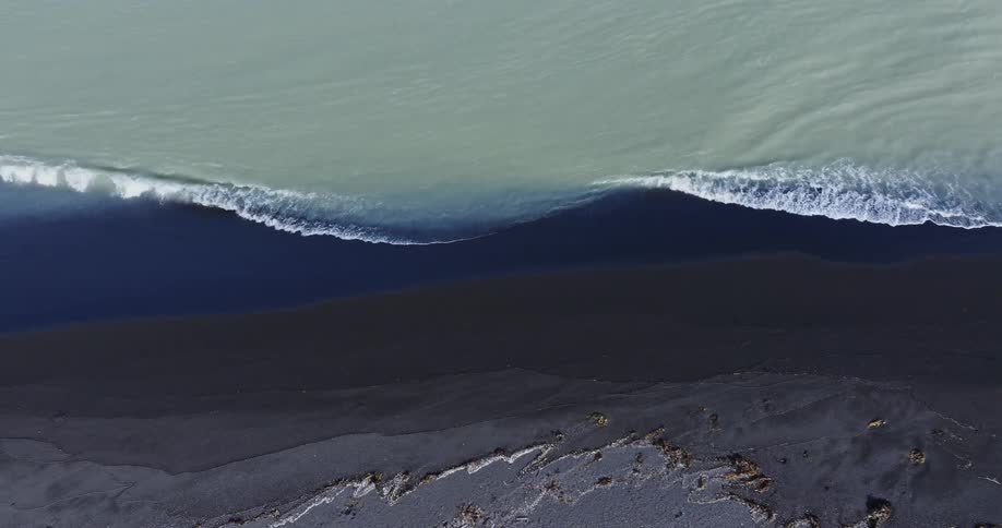 Aerial of beach coast with dark sand and gentle waves