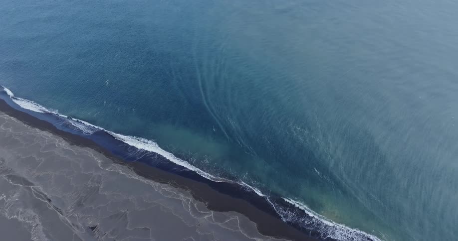Drone shot of a blue sea on the black beach