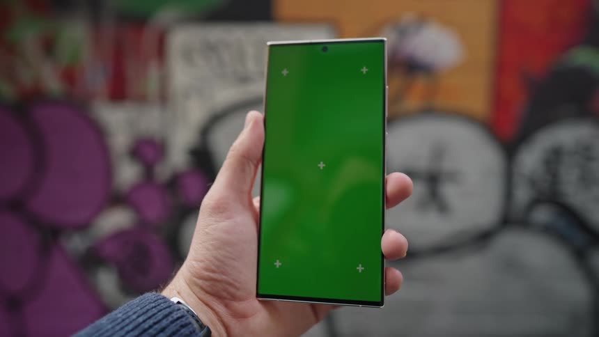 Man holding smartphone stands near mural covered building wall