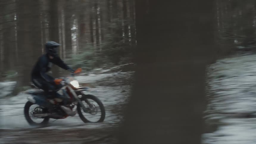 A person doing motocross in the middle of a forest with snow on the ground
