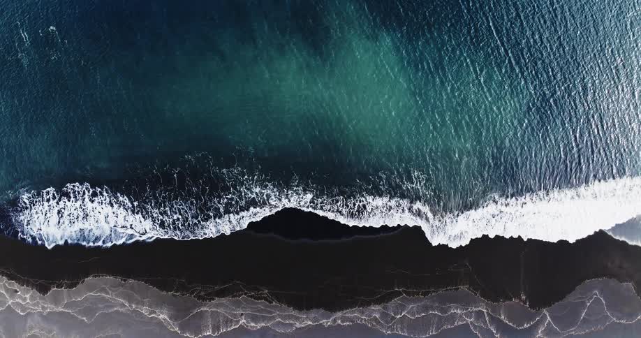 Waves from the sea hitting the shoreline where there are dark rocks