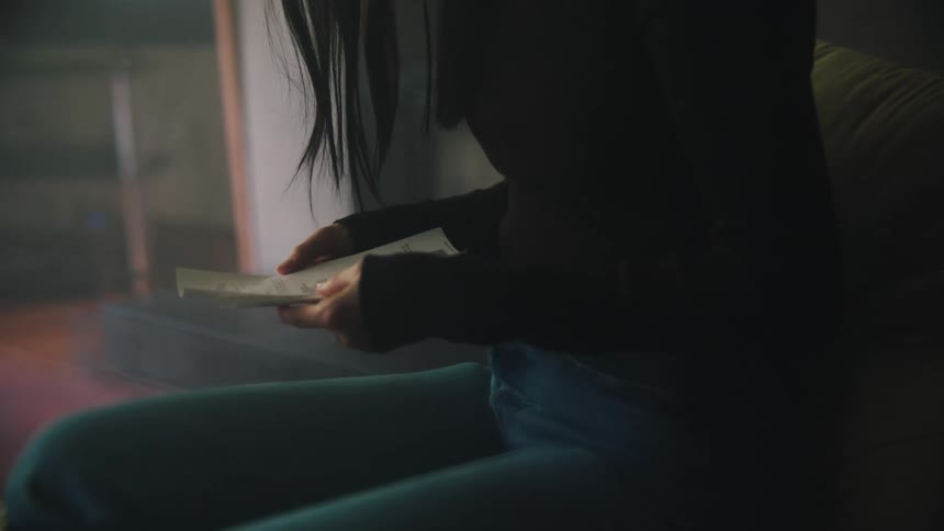A woman is sitting down holding her cell phone and looking at a piece of paper