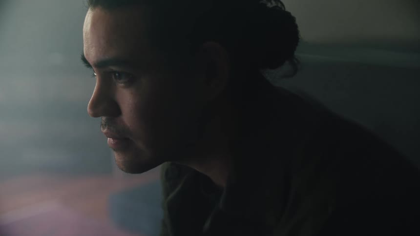 A man with a ponytail looks straight ahead and then at the ground
